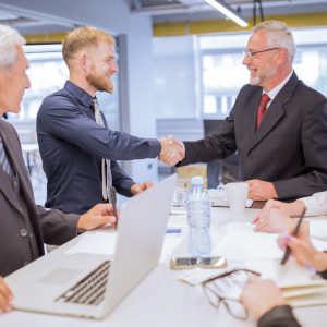 businesspeople-looking-two-businessmen-shaking-hands-business-meeting